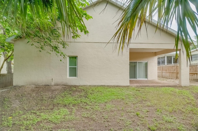 rear view of property featuring fence, a lawn, and stucco siding