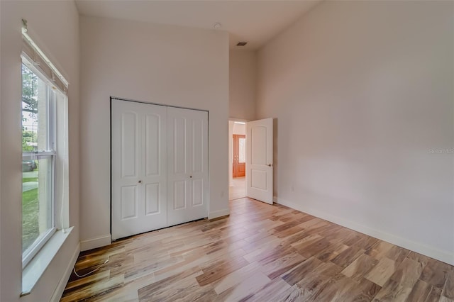 unfurnished bedroom featuring light hardwood / wood-style floors, a closet, and a towering ceiling