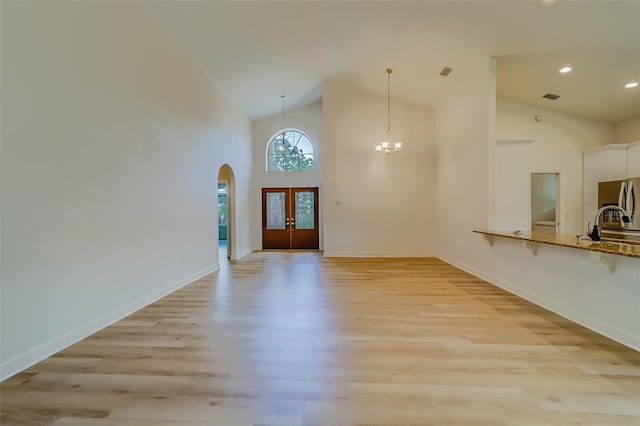 unfurnished living room with an inviting chandelier, light hardwood / wood-style flooring, sink, and high vaulted ceiling