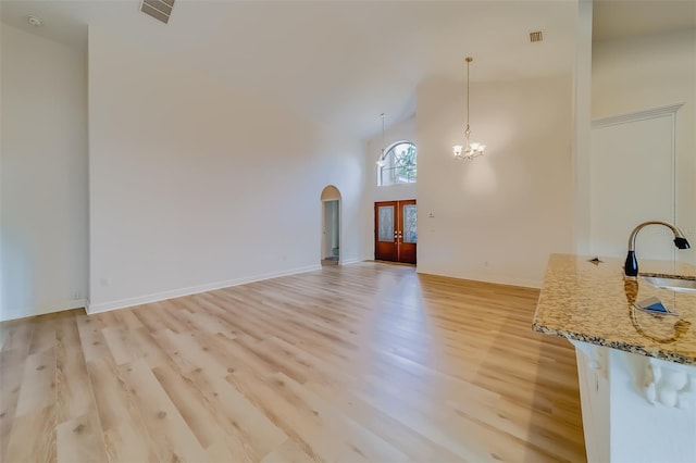 unfurnished living room with high vaulted ceiling, sink, light wood-type flooring, and a chandelier