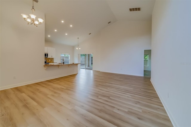 unfurnished living room featuring high vaulted ceiling, light wood-type flooring, and a notable chandelier