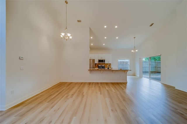 unfurnished living room featuring a towering ceiling, light hardwood / wood-style flooring, and a chandelier