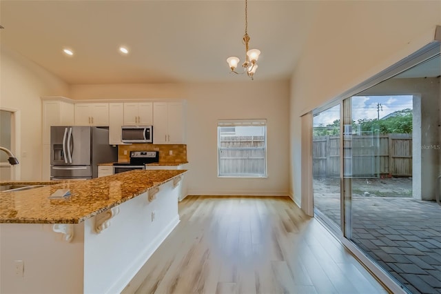 kitchen featuring stainless steel appliances, hanging light fixtures, stone counters, white cabinets, and light wood-type flooring