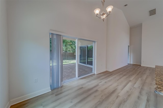 spare room featuring light hardwood / wood-style flooring, high vaulted ceiling, and an inviting chandelier