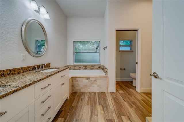 bathroom featuring a relaxing tiled tub, vanity, hardwood / wood-style flooring, and toilet