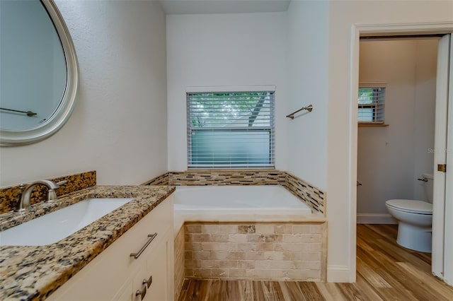 bathroom with tiled tub, vanity, a wealth of natural light, and toilet