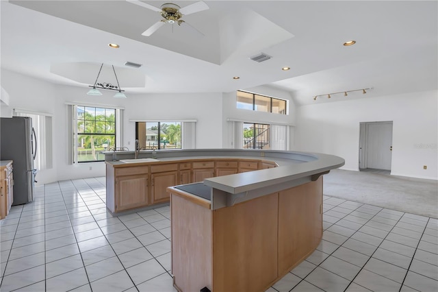 kitchen with sink, light tile patterned floors, stainless steel fridge, a tray ceiling, and an island with sink