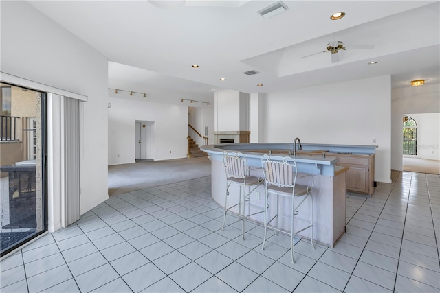 kitchen featuring light tile patterned floors, ceiling fan, a kitchen island with sink, a kitchen bar, and light brown cabinetry