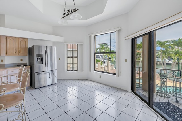 kitchen featuring a water view, stainless steel fridge with ice dispenser, hanging light fixtures, light tile patterned floors, and a tray ceiling