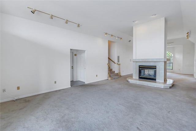 unfurnished living room featuring light carpet, high vaulted ceiling, track lighting, and a tile fireplace