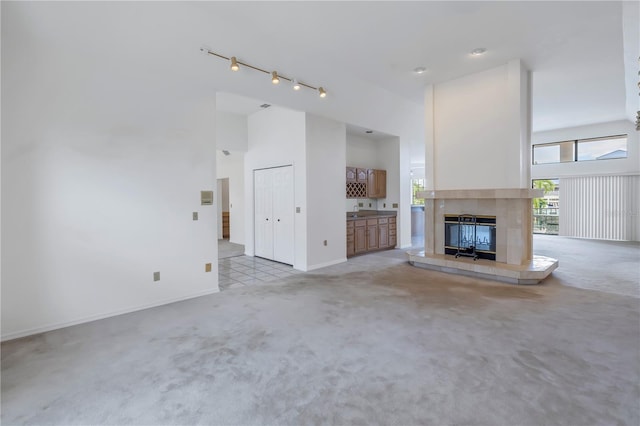 unfurnished living room featuring light colored carpet, rail lighting, high vaulted ceiling, and a fireplace