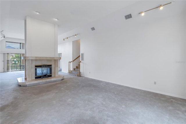 unfurnished living room featuring track lighting, high vaulted ceiling, a tile fireplace, and concrete floors