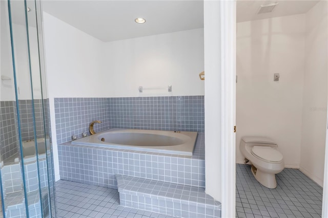 bathroom featuring a relaxing tiled tub, tile patterned floors, and toilet