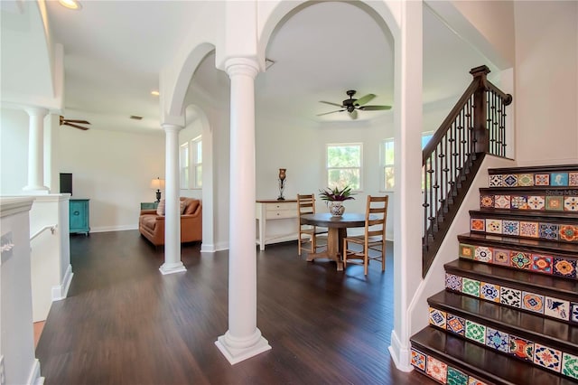 stairway with decorative columns, ceiling fan, and dark wood-type flooring