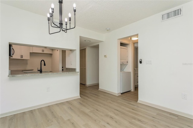 kitchen featuring stacked washer / drying machine, light hardwood / wood-style floors, a textured ceiling, and tasteful backsplash