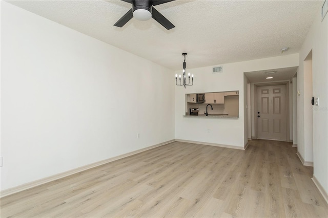 unfurnished living room featuring sink, ceiling fan with notable chandelier, a textured ceiling, and light wood-type flooring