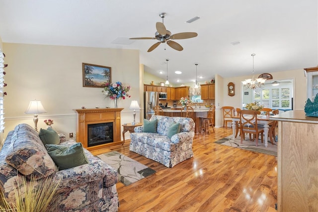 living room featuring light hardwood / wood-style flooring, vaulted ceiling, and ceiling fan with notable chandelier