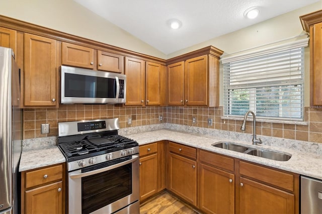 kitchen featuring lofted ceiling, stainless steel appliances, sink, and light stone counters