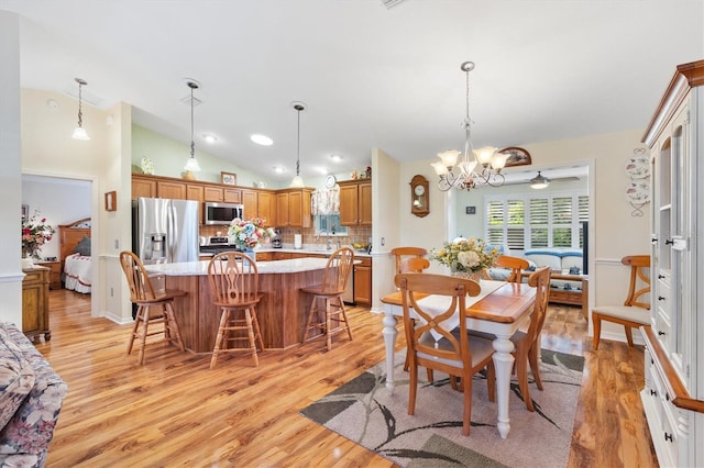 dining space with lofted ceiling, light wood-type flooring, and ceiling fan with notable chandelier