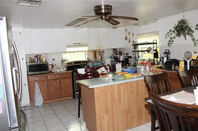 kitchen with white cabinets, backsplash, light tile patterned floors, ceiling fan, and stainless steel appliances