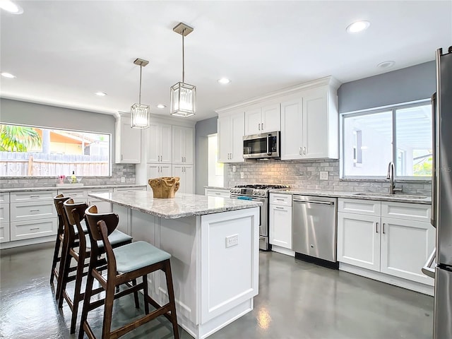 kitchen with stainless steel appliances, sink, white cabinets, a kitchen island, and hanging light fixtures