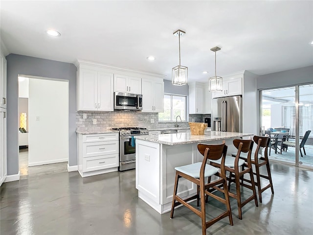 kitchen featuring light stone countertops, stainless steel appliances, decorative light fixtures, white cabinets, and a center island