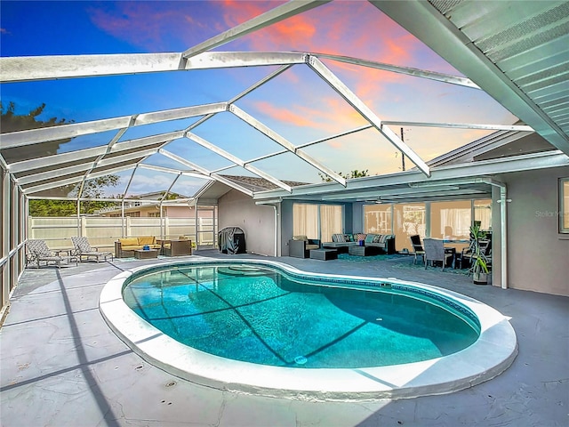 pool at dusk with an outdoor hangout area, glass enclosure, and a patio