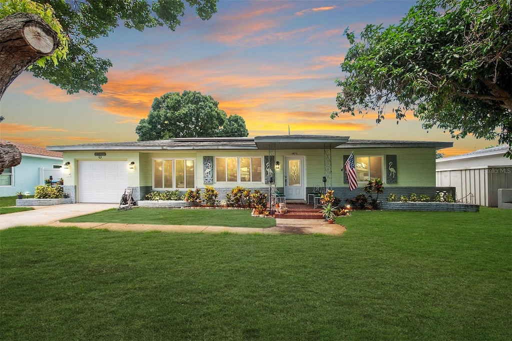 ranch-style home with a garage, concrete driveway, and a lawn