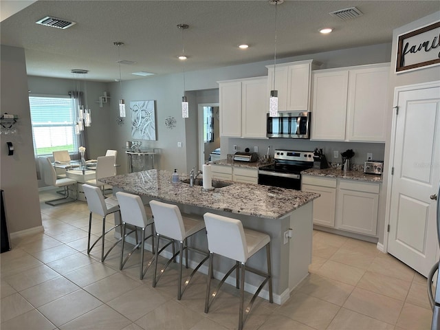 kitchen featuring sink, appliances with stainless steel finishes, an island with sink, white cabinets, and light stone counters