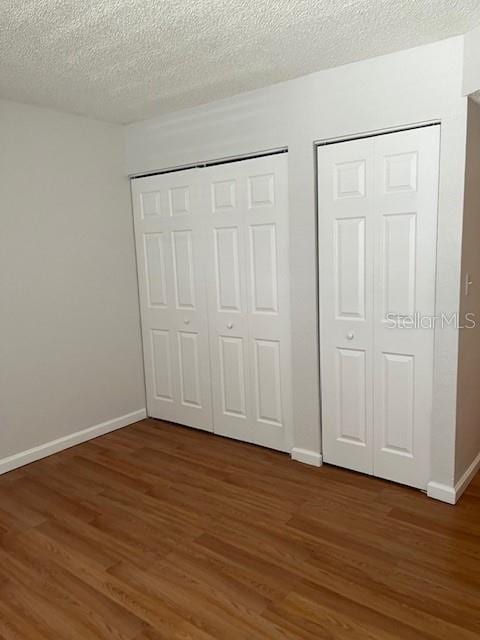 unfurnished bedroom featuring dark wood-type flooring, multiple closets, and a textured ceiling