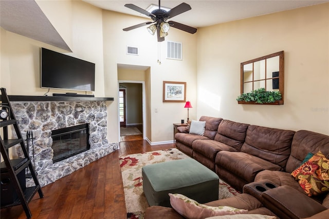 living room with dark wood-type flooring, a stone fireplace, and ceiling fan