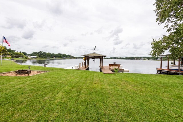 dock area with an outdoor fire pit, a water view, and a lawn