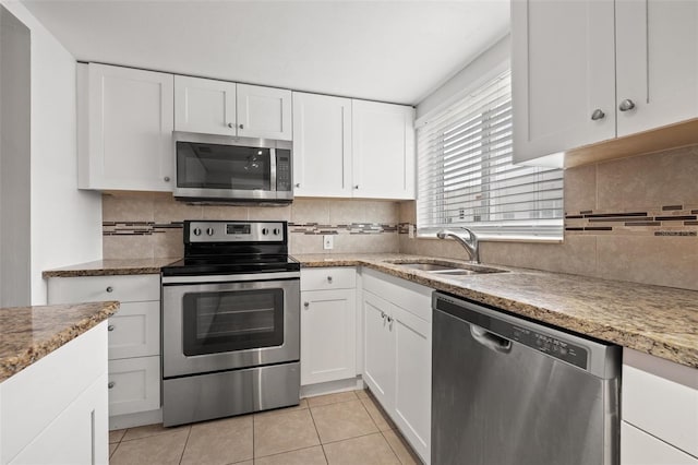 kitchen featuring appliances with stainless steel finishes, backsplash, sink, light tile patterned floors, and white cabinets