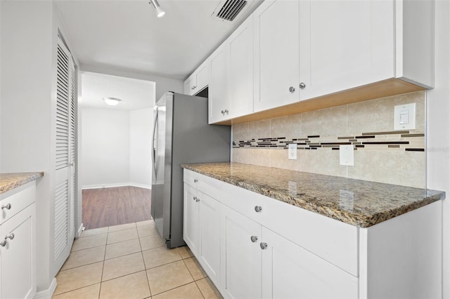 kitchen with white cabinets, light tile patterned floors, stone countertops, and stainless steel refrigerator