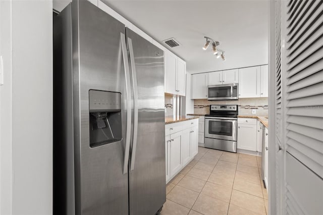 kitchen with light stone countertops, light tile patterned floors, backsplash, white cabinets, and appliances with stainless steel finishes