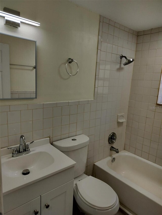 full bathroom with vanity, tile walls, tiled shower / bath combo, toilet, and backsplash