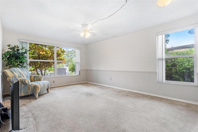 unfurnished room featuring carpet floors, a wainscoted wall, a textured ceiling, and a ceiling fan