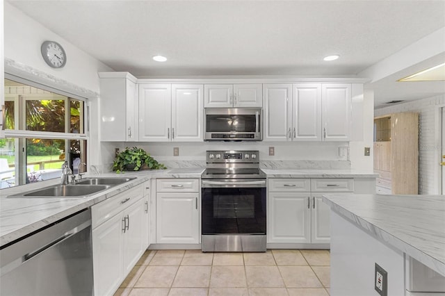 kitchen featuring appliances with stainless steel finishes, white cabinets, a sink, and light tile patterned flooring