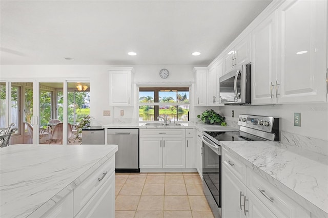 kitchen featuring light stone counters, light tile patterned floors, stainless steel appliances, white cabinetry, and a sink