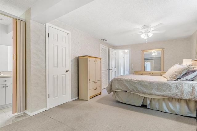 bedroom with light colored carpet, visible vents, ensuite bathroom, a textured ceiling, and baseboards