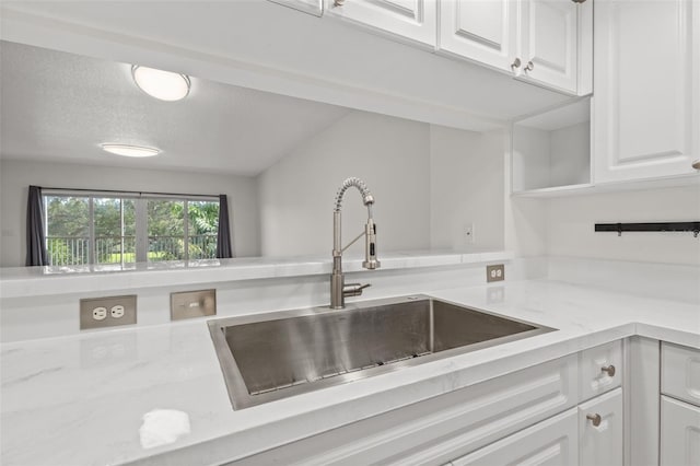 kitchen featuring light stone countertops, sink, white cabinets, and a textured ceiling