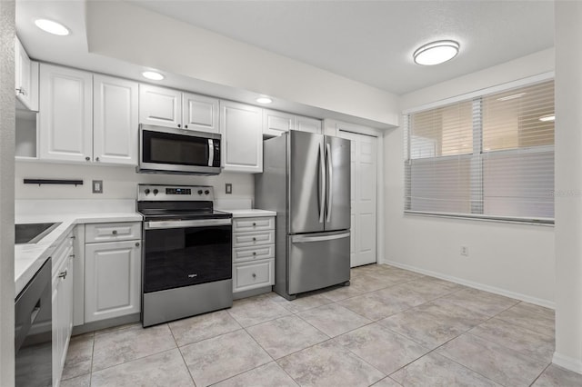 kitchen with light tile patterned floors, light countertops, appliances with stainless steel finishes, white cabinetry, and baseboards