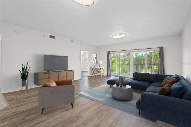 living room with baseboards, a textured ceiling, visible vents, and wood finished floors