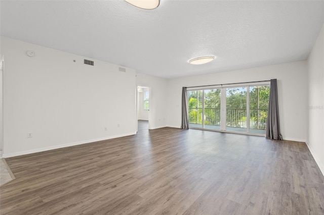 unfurnished room with visible vents, a textured ceiling, baseboards, and wood finished floors