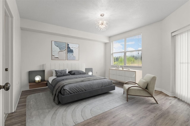 bedroom featuring a chandelier, a textured ceiling, baseboards, and wood finished floors