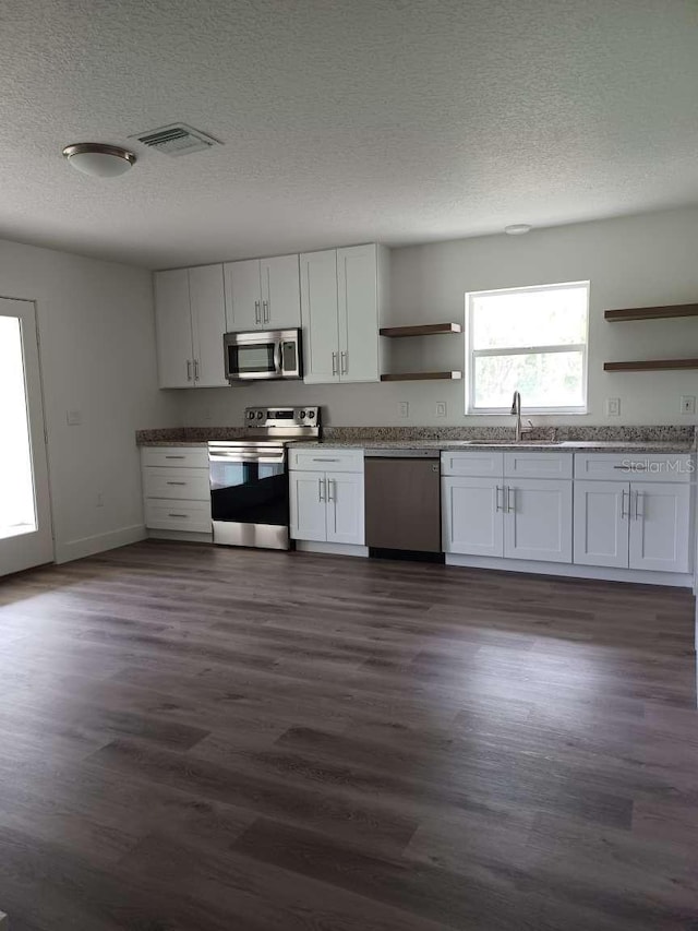 kitchen with stainless steel appliances, white cabinetry, and dark hardwood / wood-style floors