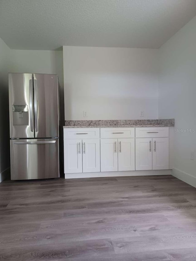 kitchen with light stone counters, white cabinets, a textured ceiling, stainless steel refrigerator with ice dispenser, and light hardwood / wood-style floors