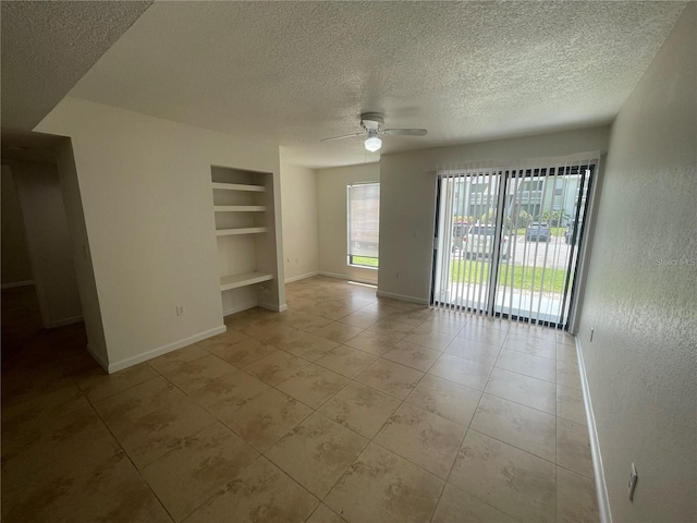 tiled empty room with a textured ceiling, built in features, and ceiling fan