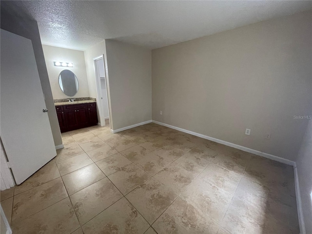 interior space featuring ensuite bathroom, sink, light tile patterned flooring, and a textured ceiling