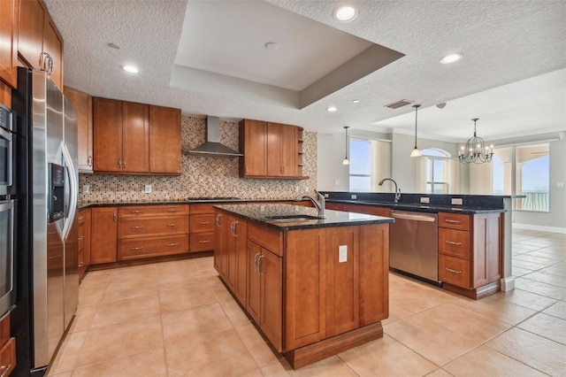 kitchen featuring appliances with stainless steel finishes, pendant lighting, an island with sink, sink, and wall chimney range hood